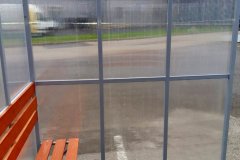 Навес-курилка с поликарбонатными стенками на металлическом каркасе и деревянной скамьёй на парковке