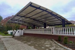 Arkveida nojume divām automašīnām ar polikarbonāta jumtu uz metāla karkasa pie mājas