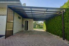 Vienslīpju polikarbonāta nojume automašīnai uz metāla karkasa mājas pagalmā.