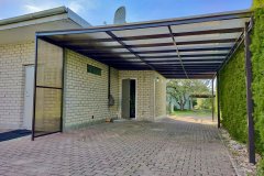 Vienslīpju nojume mājai ar polikarbonāta jumtu uz metāla karkasa pagalmā