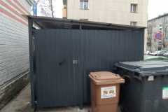 Mājas nojume ar metāla karkasu un polikarbonāta jumtu pagalmā pie atkritumu konteineriem.