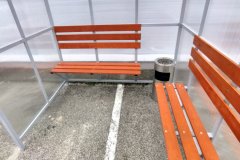 Smēķēšanas nojumes iekšiene ar diviem koka soliņiem un metāla pelnu trauku