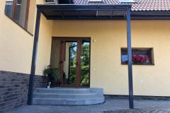 Polikarbonāta nojume uz metāla karkasa pie mājas ieejas.